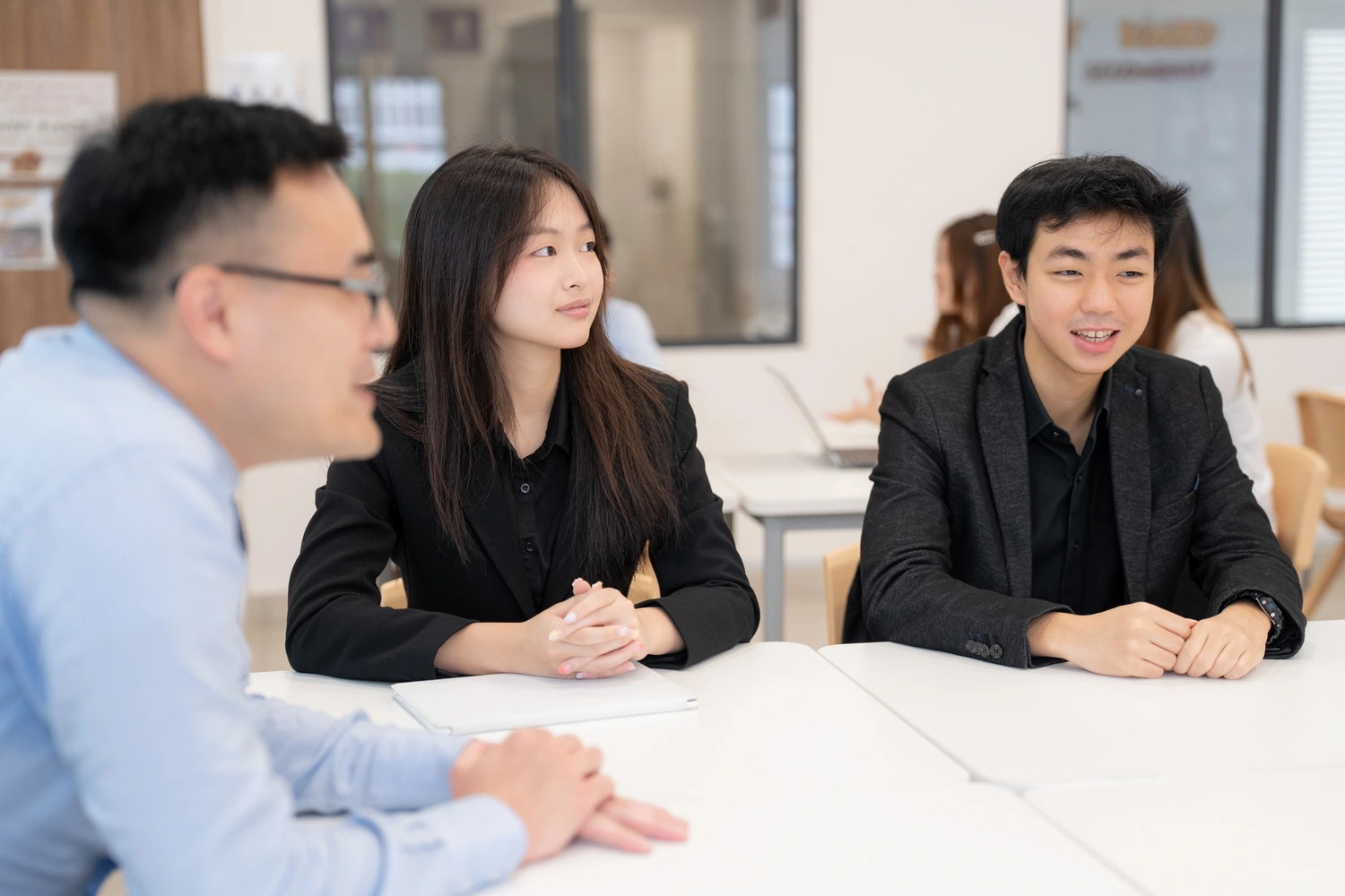Three students in conversation across a table, mid-discussion.