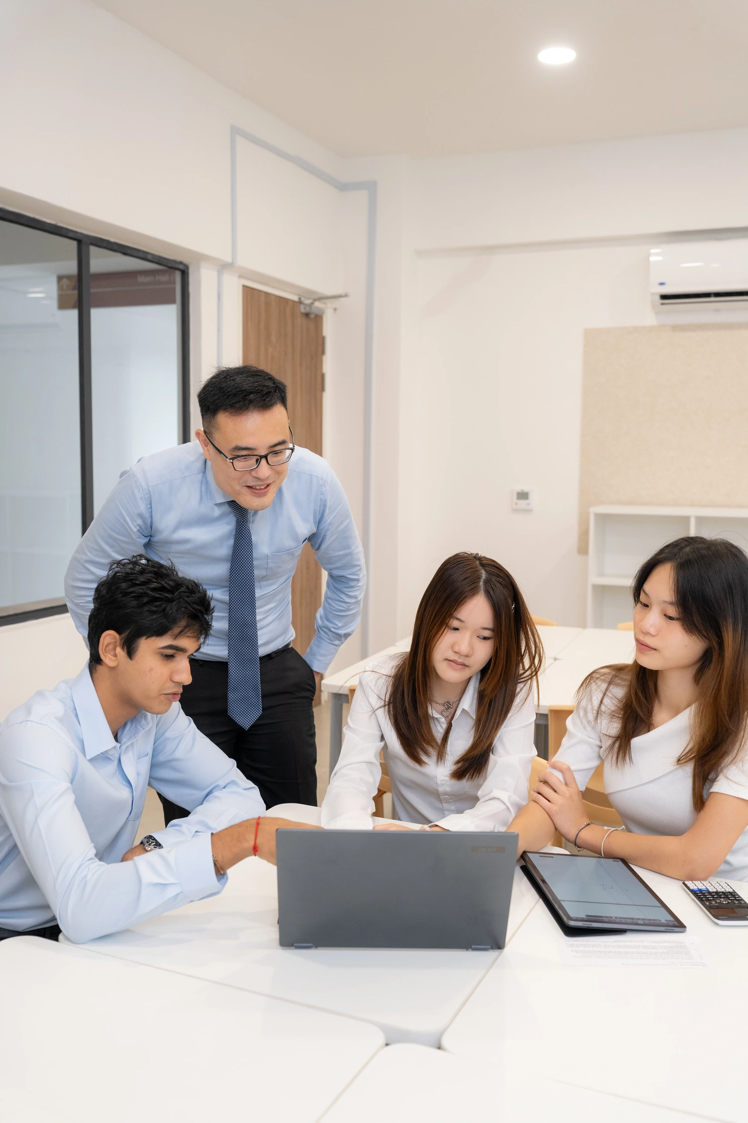 A tutor helps students working on a laptop.