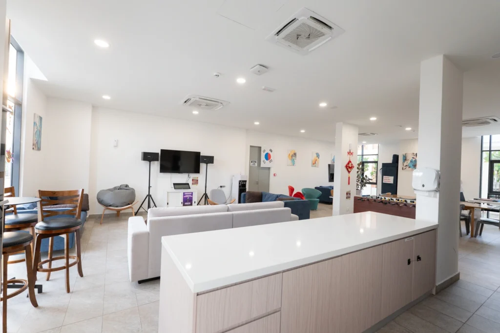 The boarding house common lounge with sofas, karaoke setup and a shared kitchen bar.