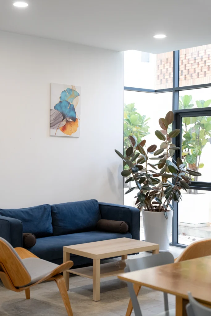 A quiet lounge corner with a sofa, armchair and plants by a large window.
