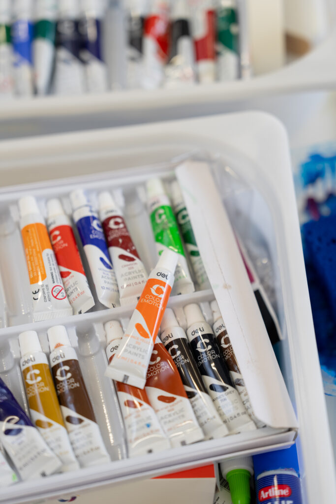 A collection of colorful acrylic paint tubes neatly arranged in a white plastic tray.