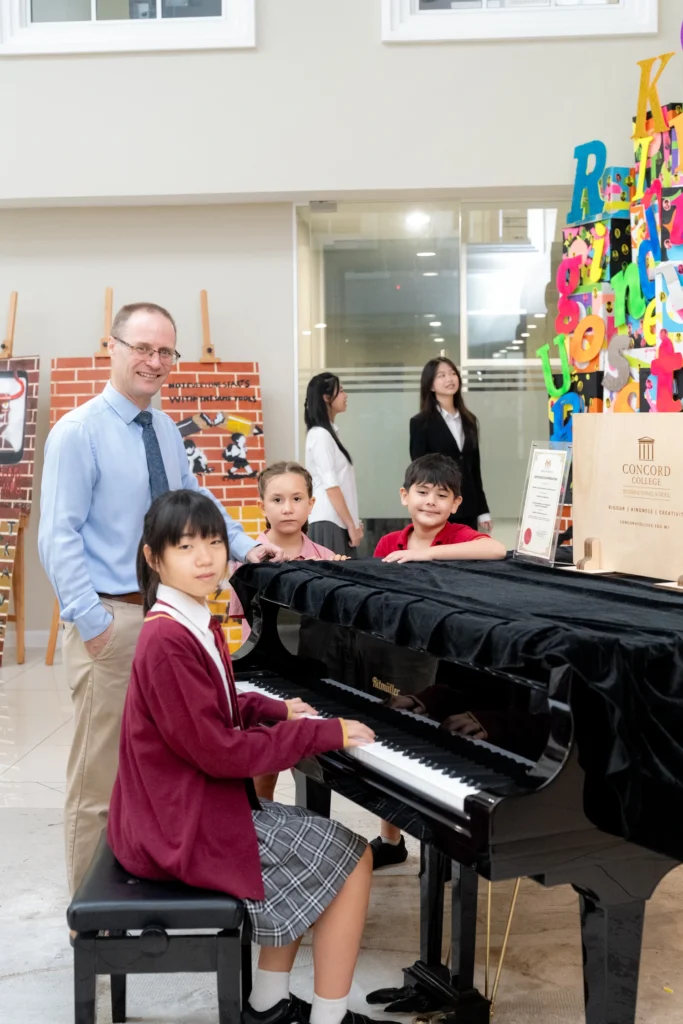 A student plays the piano while the Executive Principal watches.