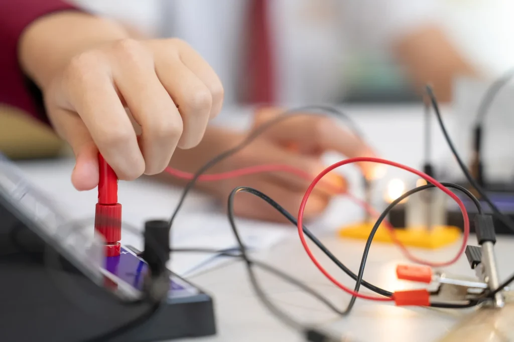 A student's hands connecting a circuit with leads during a physics investigation.
