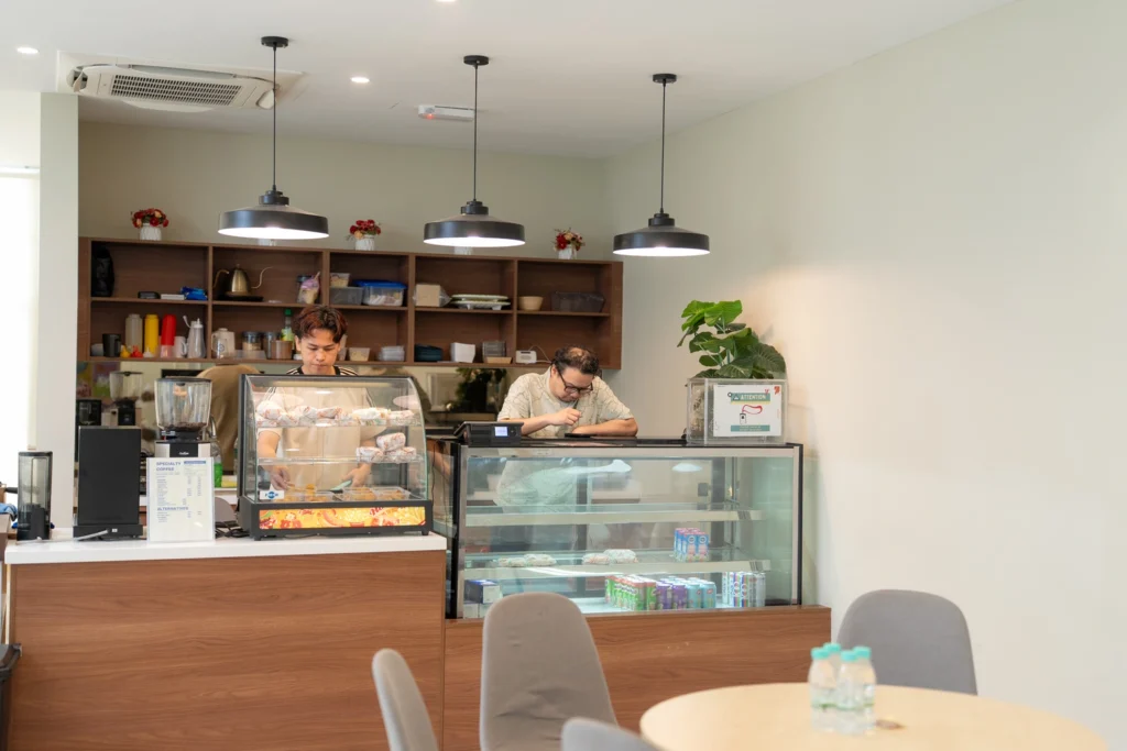 Two individuals working behind the counter of a cafe with a display case containing baked goods.