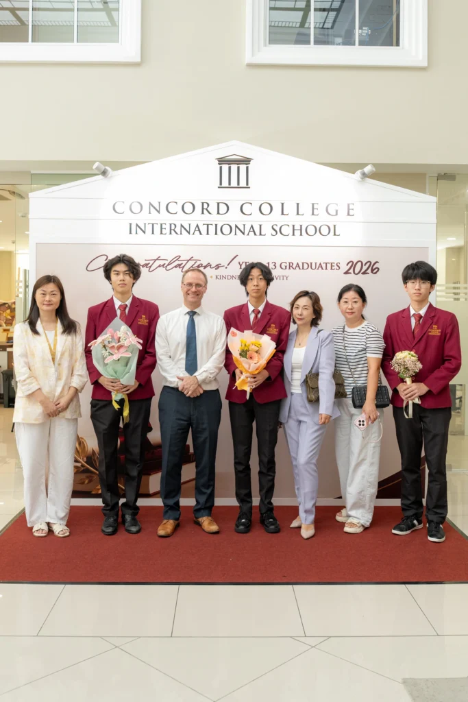 Graduates and staff line up at the Concord College graduation backdrop.
