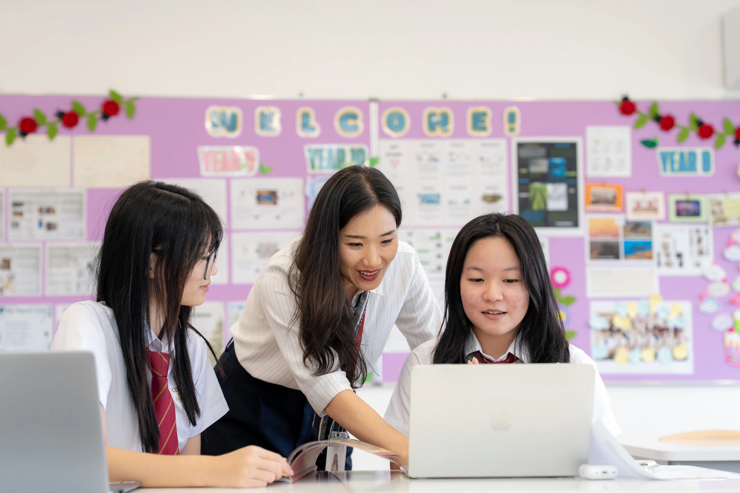 Two students work at a laptop with their teacher in front of a Year 8 classroom display.