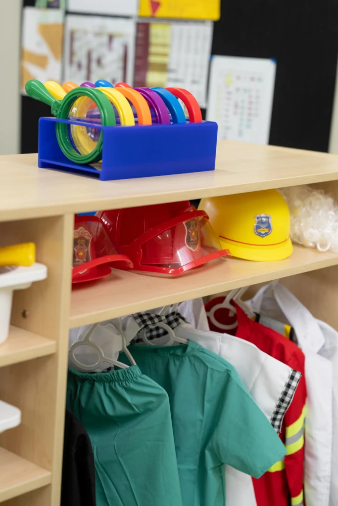 Dressing-up clothes and sorting toys on open shelving in an Early Years classroom.