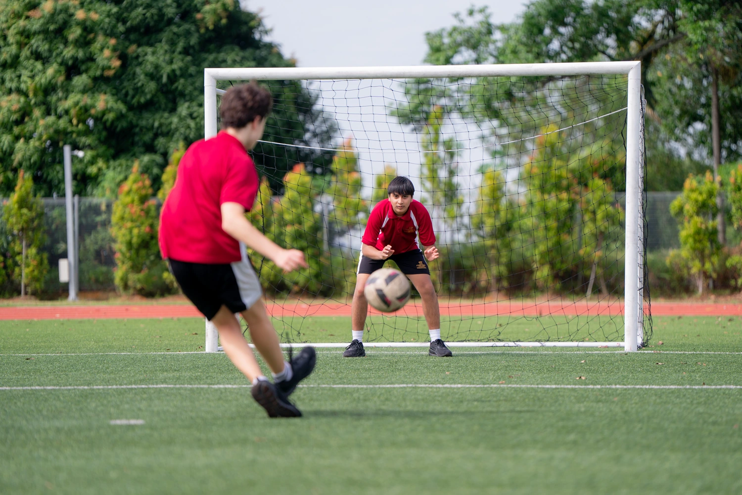 A student shoots at goal on the football pitch as the goalkeeper prepares to save.