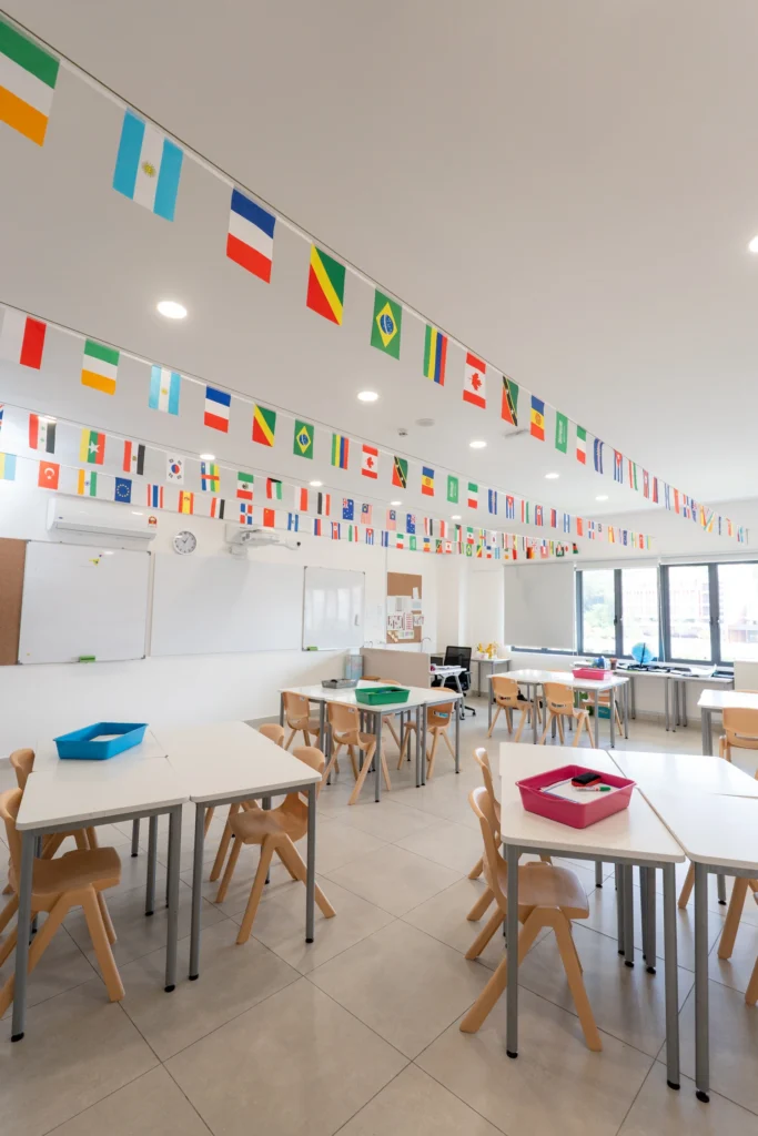 A secondary geography classroom with group tables and international flags strung across the ceiling.