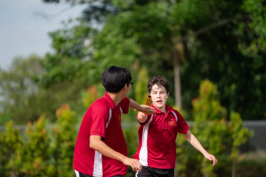 A student passes the baton to a teammate during a relay on the school field.