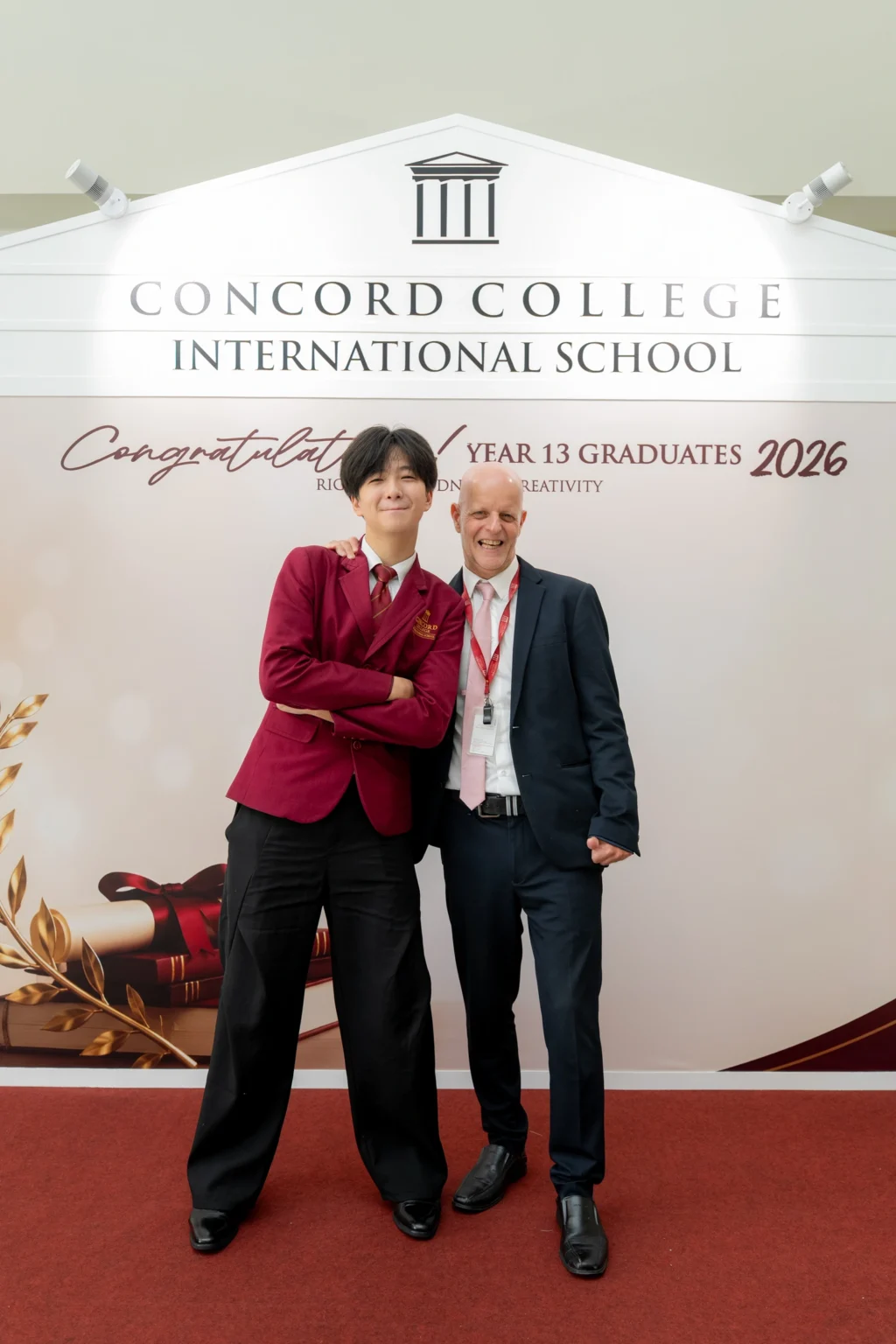 Two individuals in formal attire standing in front of a backdrop celebrating Concord College International School's Year 13 Graduates 2026.